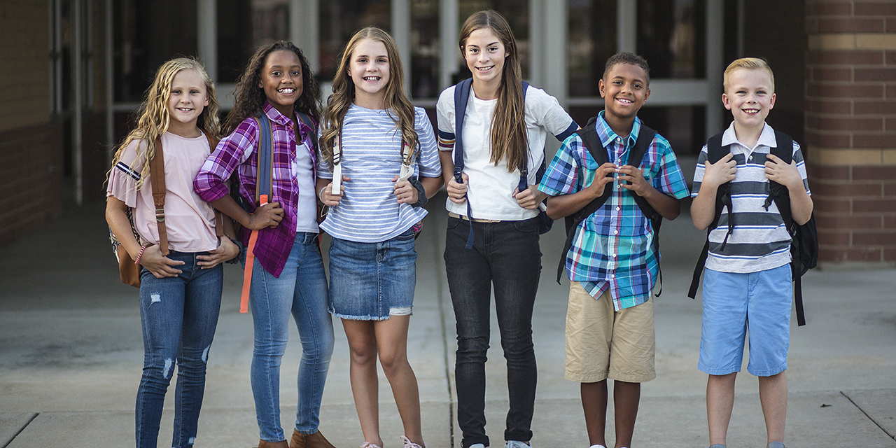 Group of students carrying backpacks standing in front of a school.