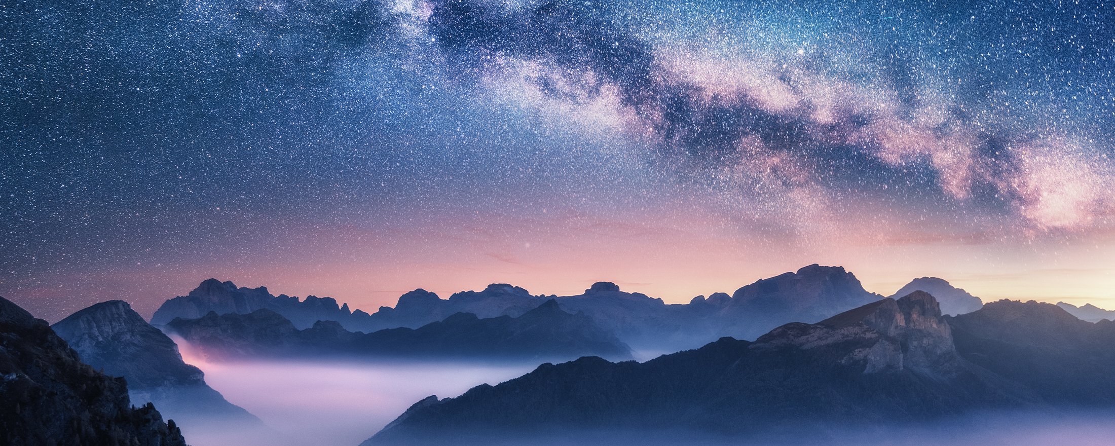 Milky Way over mountains and misty valleys at dawn under a starry sky.